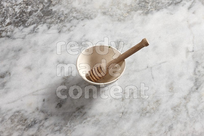 Beige Pottery Bowl with wooden honey handle in it, on grey marble flooring, 65 degree angle