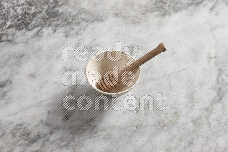 Beige pottery bowl with wooden honey dipper in it on grey marble background