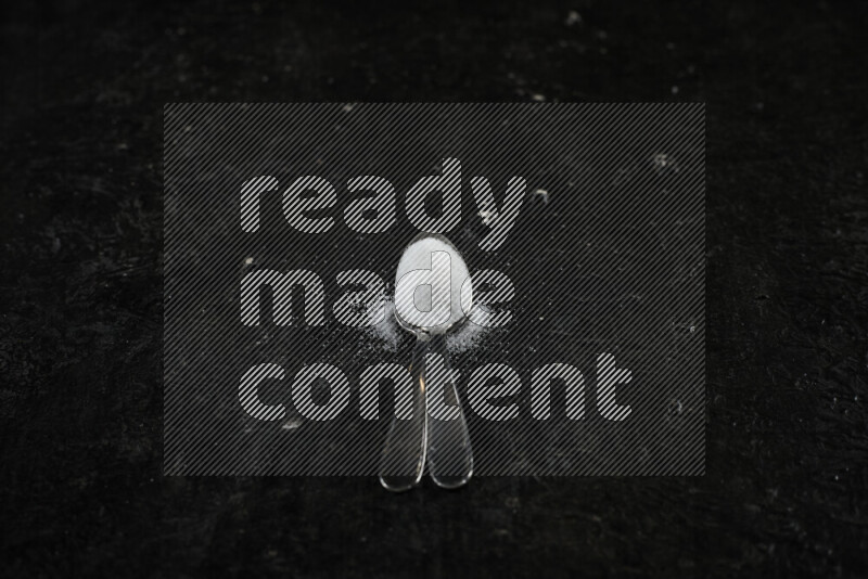 ملعقتان معدنيتان ممتلئتان بالملح الأبيض على خلفية سوداء