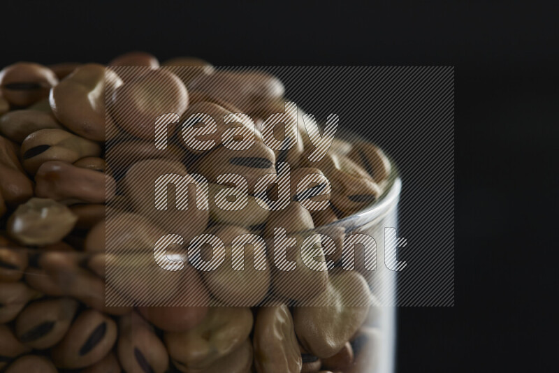 Fava beans in a glass jar on black background