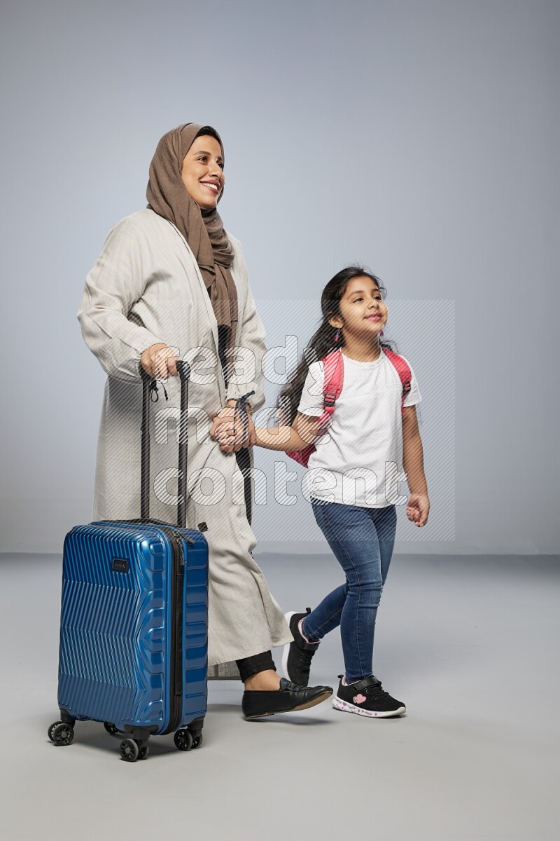 Mom and daughter standing pulling a carry-on bag on gray background