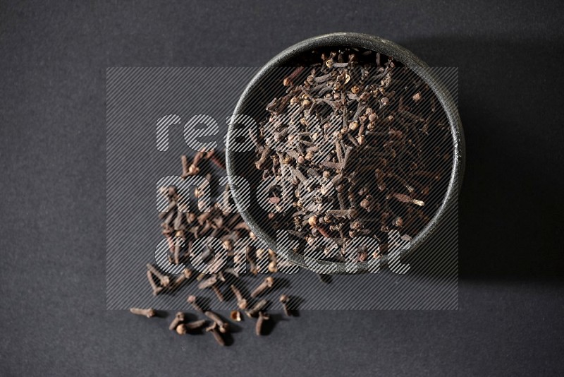 A black pottery bowl full of cloves on a black flooring