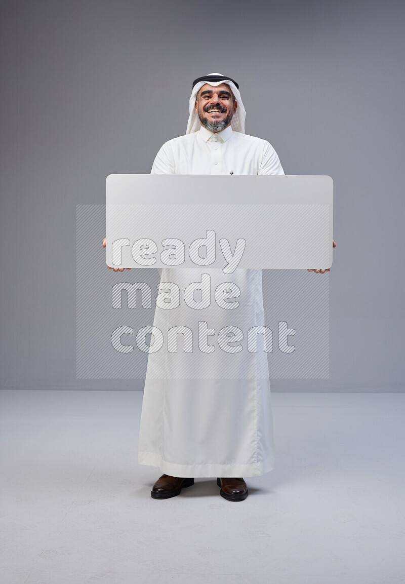 Saudi man Wearing Thob and white Shomag standing holding board on Gray background