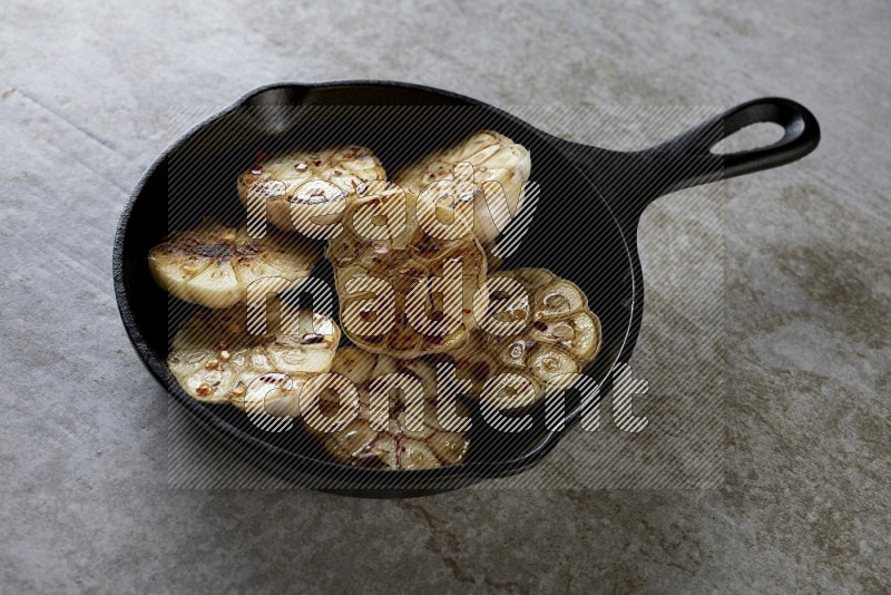 half's roasted garlic in a black pan on a grey textured countertop