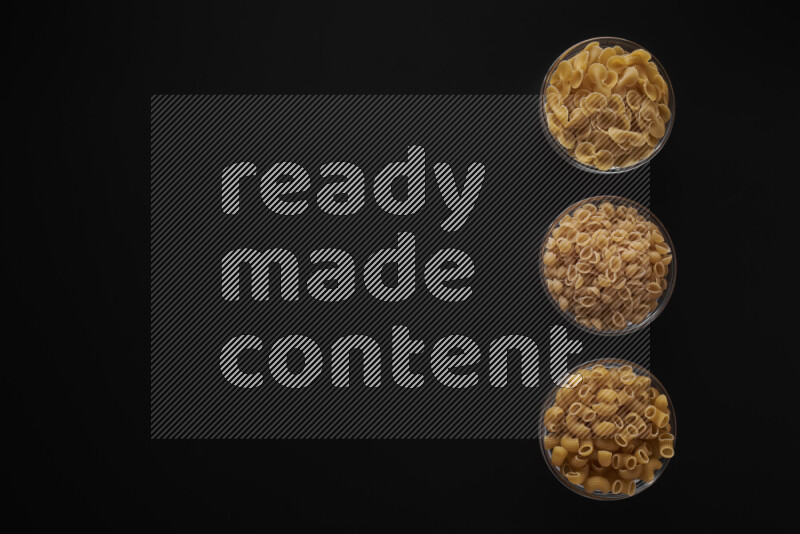 Different pasta types in 3 glass bowls on black background