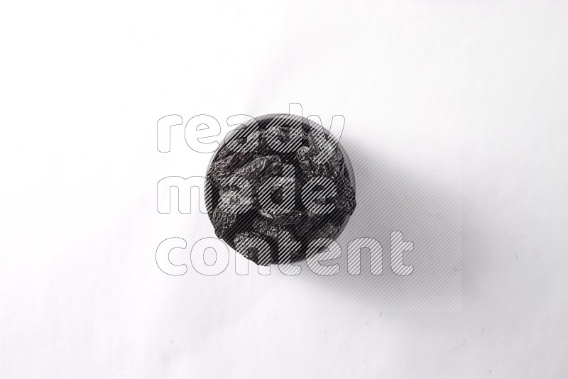 Dried plums in a black pottery bowl on white background