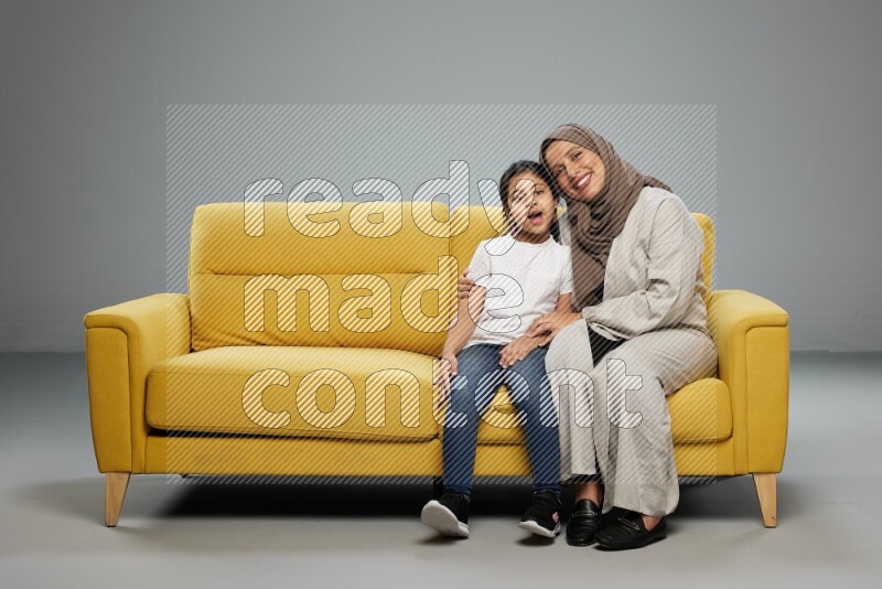 A girl with her mother sitting and interacting with the camera on gray background