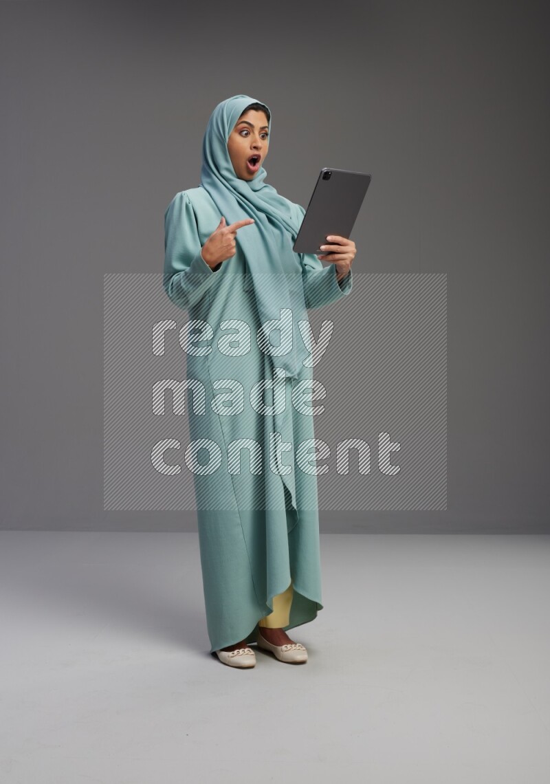 Saudi Woman wearing Abaya standing working on tablet on Gray background