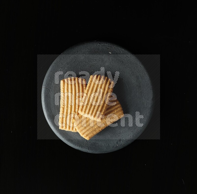 Golden biscuits in a black pottery plate on black background