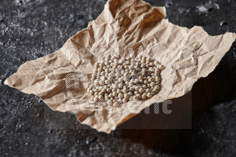 White pepper beads in a crumpled piece of on textured black flooring