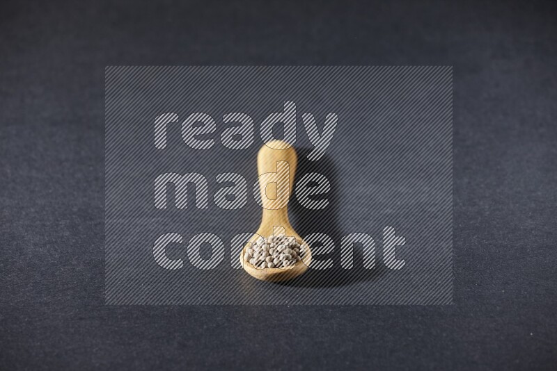 A wooden spoon full of white pepper beads on black flooring