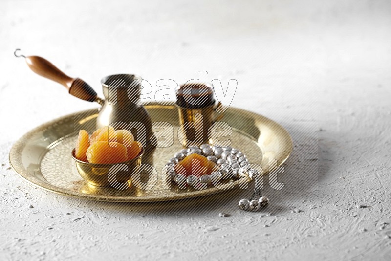 مشمش مجفف في وعاء معدني مع القهوة وسبحة على صينية علي خلفية بيضاء