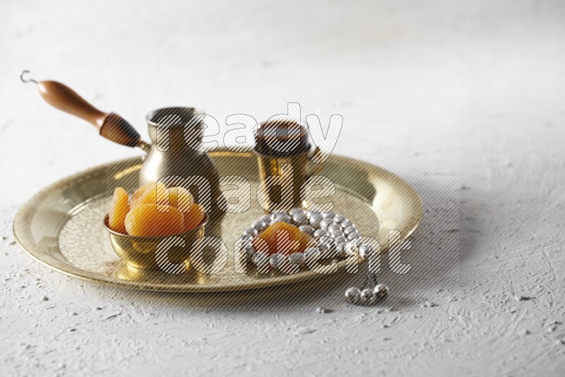 Dried apricots in a metal bowl with coffee and prayer beads on a tray in a light setup