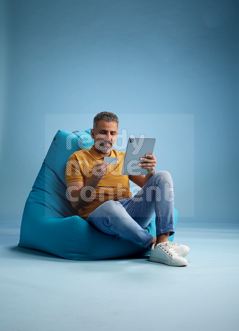 A man sitting on a blue beanbag and holding ATM card with tablet