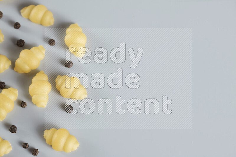 Raw pasta with different ingredients such as cherry tomatoes, garlic, onions, red chilis, black pepper, white pepper, bay laurel leaves, rosemary, cardamom and mushrooms on light blue background