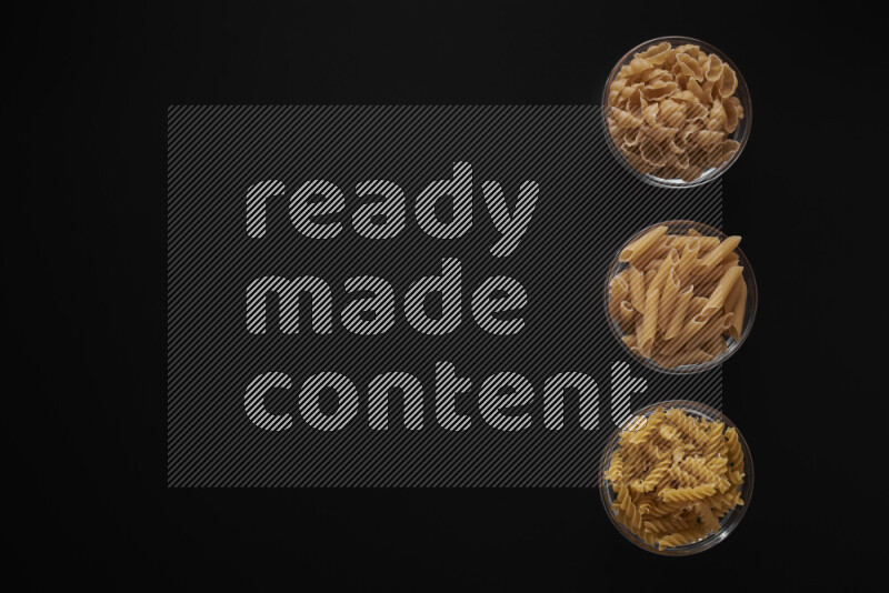 Different pasta types in 3 glass bowls on black background