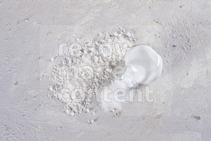 A glass jar full of table salt with some sea salt crystals beside it on a white background