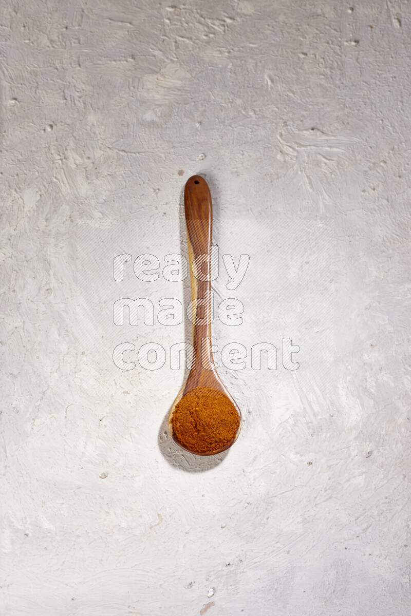 A wooden ladle full of ground paprika powder on white background