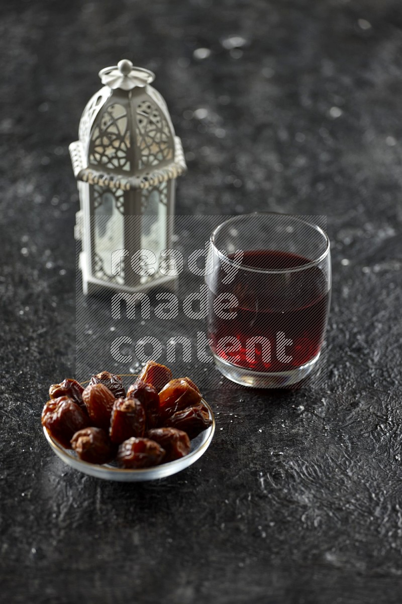 A white lantern with drinks, dates, nuts, prayer beads and quran on textured black background