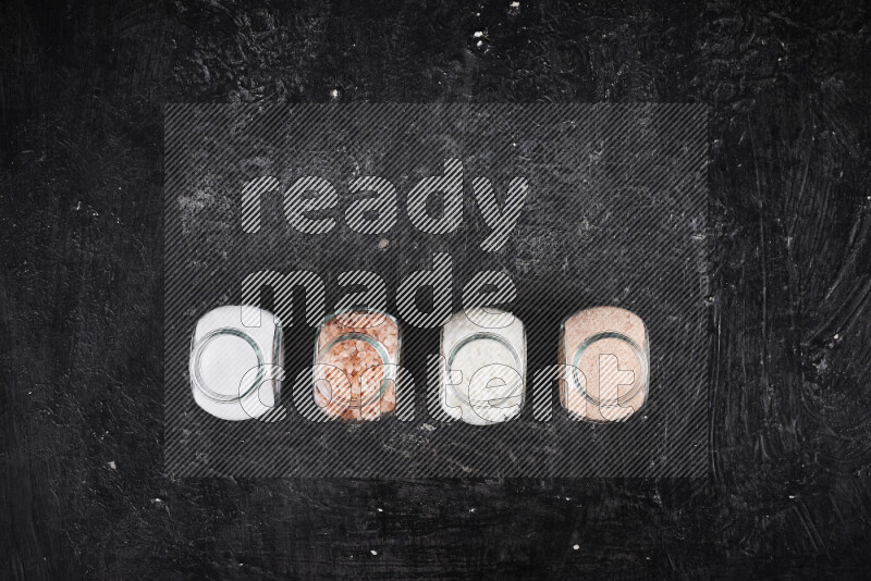 4 glass jars filled with table salt, coarse sea salt, fine himalayan salt and coarse himalayan salt on black background