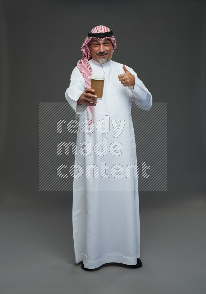 Saudi man with shomag Standing holding paper cup on gray background