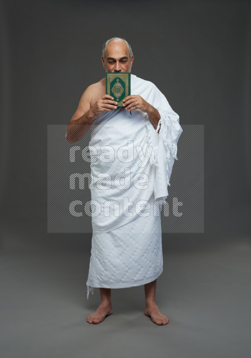 A man wearing Ehram Standing reading quran on gray background