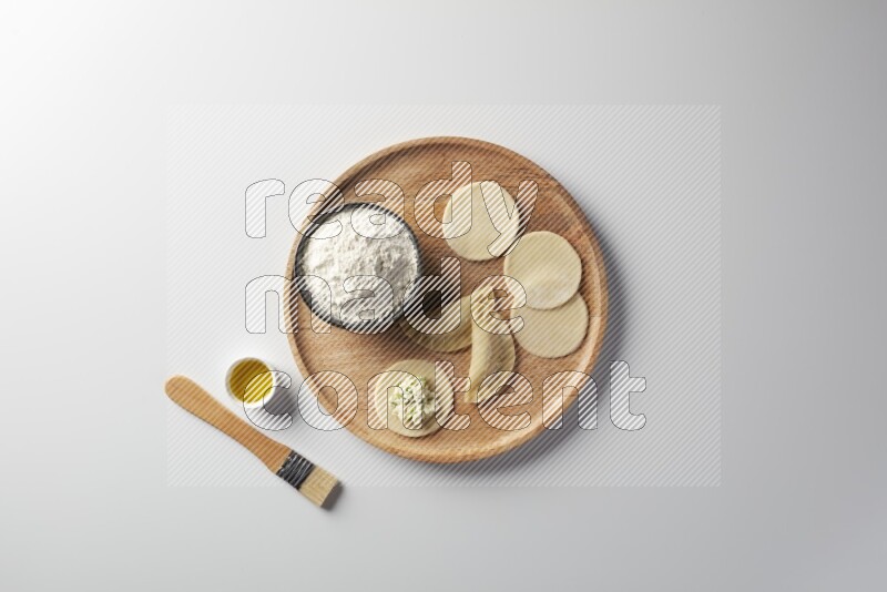 two closed sambosas and one open sambosa filled with cheese while flour, and oil with oil brush aside in a wooden dish on a white background