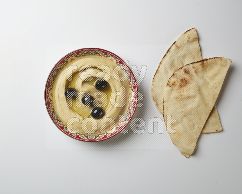 Hummus in a red plate with patterns garnished with black olives on a white background