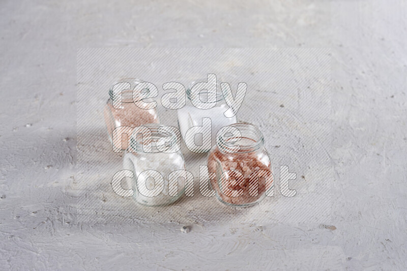 4 glass jars filled with table salt, coarse sea salt, fine himalayan salt and coarse himalayan salt on white background