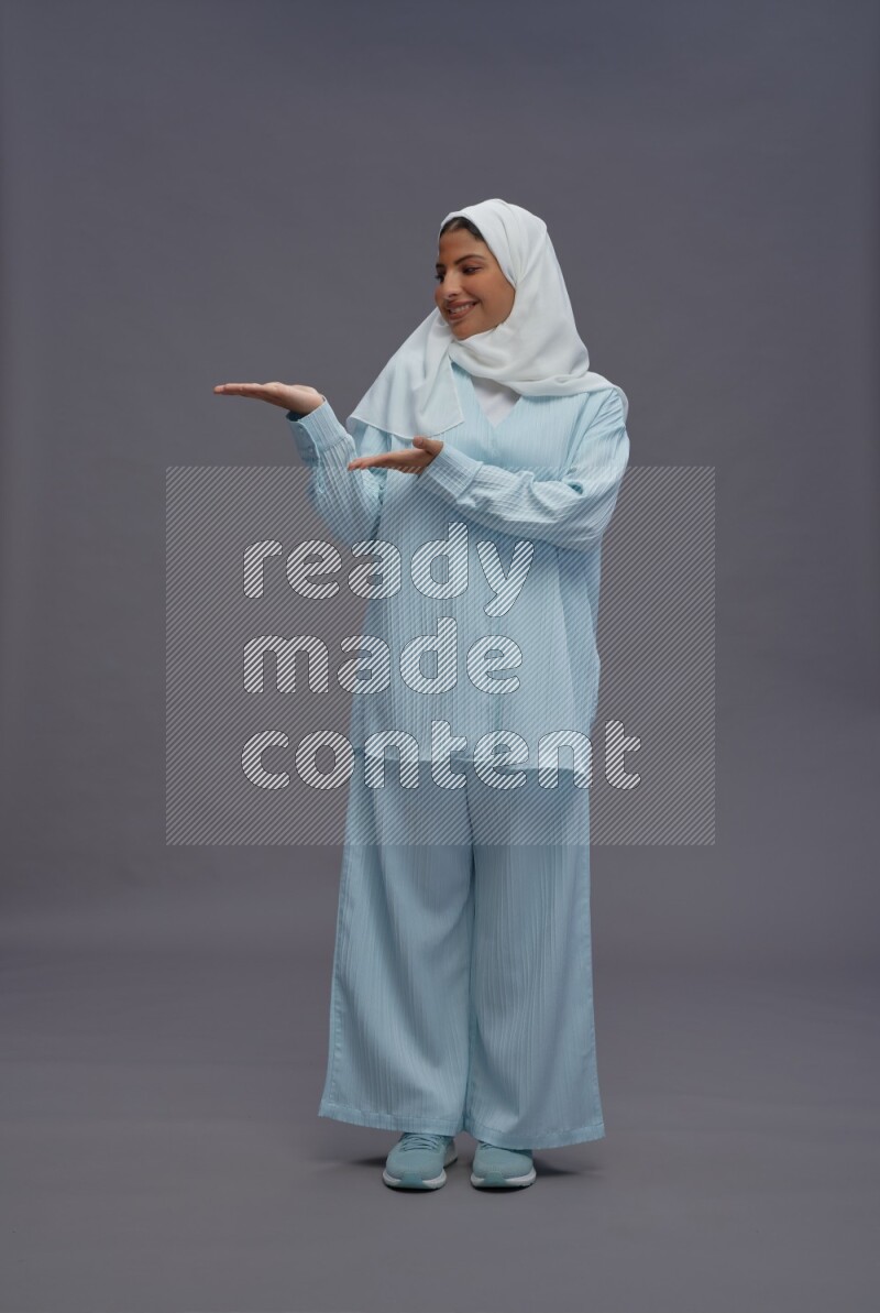 Saudi woman wearing hijab clothes standing interacting with the camera on gray background