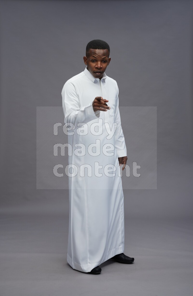 Saudi man wearing thob standing interacting with the camera on gray background