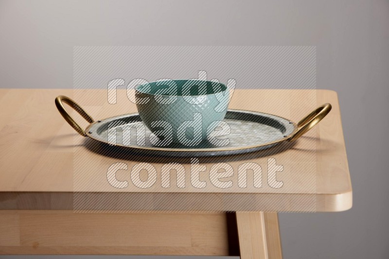 blue bowl placed on a rounded stainless steel metal tray with golden handels on the edge of wooden table