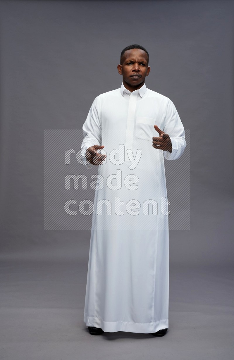 Saudi man wearing thob standing interacting with the camera on gray background