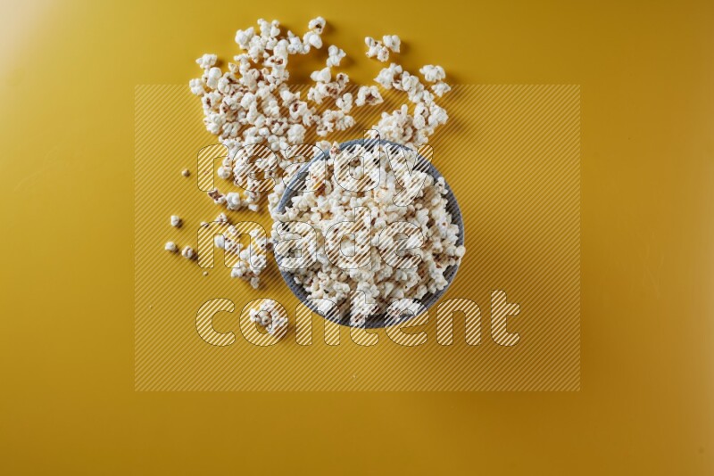 A multicolored pottery bowl full of popcorn with popcorn beside it on a yellow background in different angles