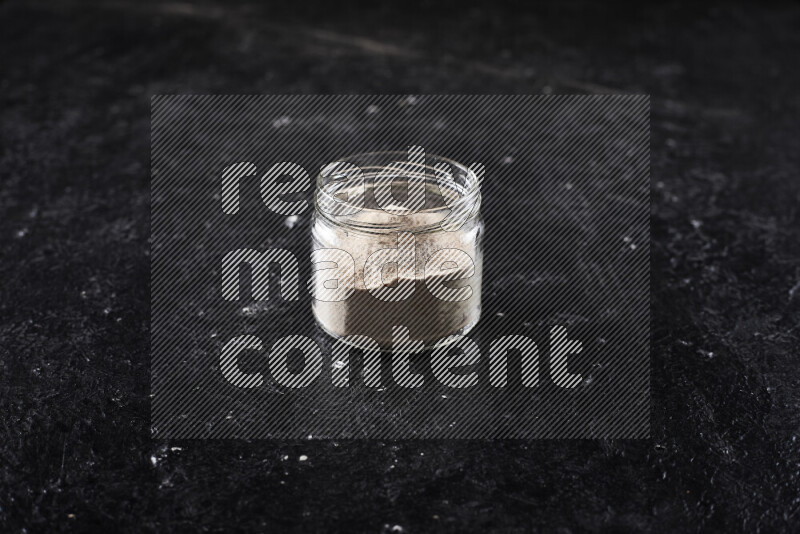 A glass jar full of onion powder on black background