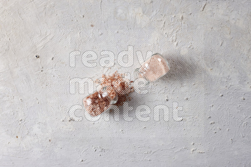 2 glass jars one is filled with fine himalayan salt and the other with coarse himalayan salt on white background