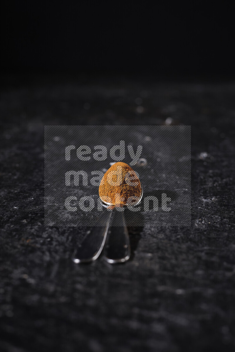 Two metal spoons full of ground paprika powder on black background