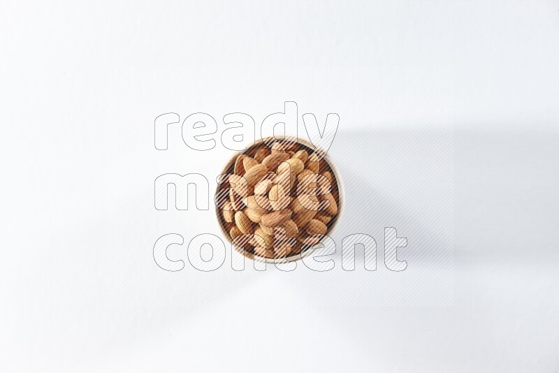 A beige ceramic bowl full of peeled almonds on a white background in different angles
