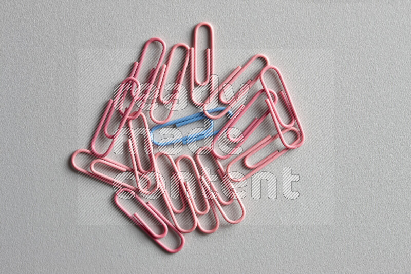A bunch of pink paper clips with a different colored paper clip in the center on grey background