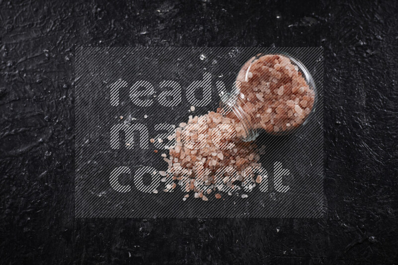 A glass jar full of coarse himalayan salt crystals on black background