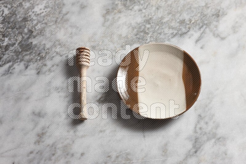Multicolored pottery plate with wooden honey dipper on the side on grey marble background