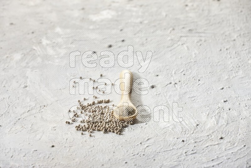A wooden spoon full of white pepper powder and white pepper beads on textured white flooring
