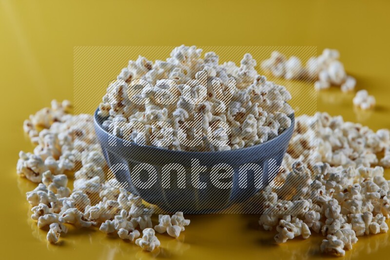 A blue pottery bowl full of popcorn with popcorn beside it on a yellow background in different angles