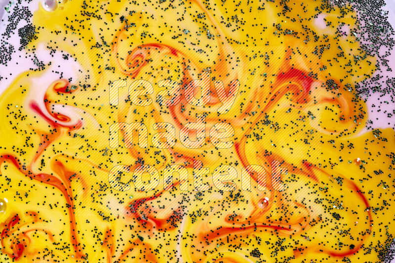 A close-up of sparkling green glitter scattered on swirling yellow, red and pink background