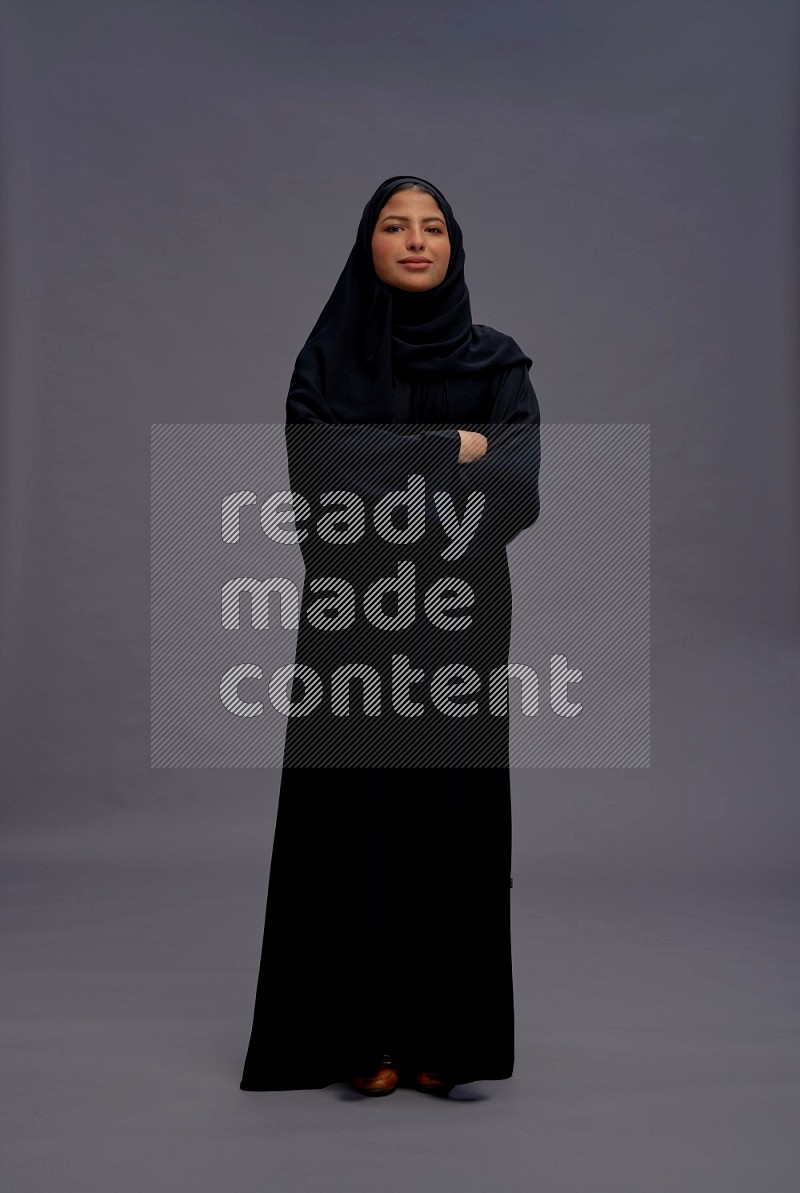 Saudi woman wearing Abaya standing with crossed arms on gray background
