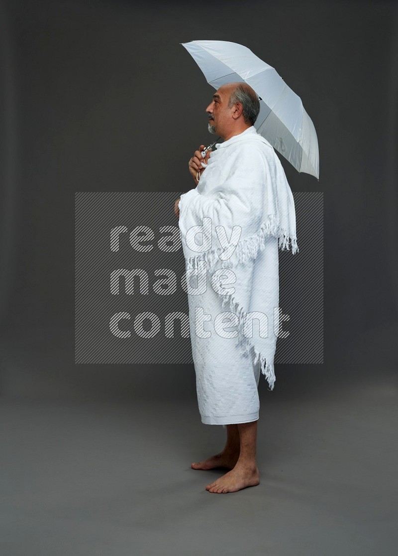 A man wearing Ehram Standing holding umbrella on gray background
