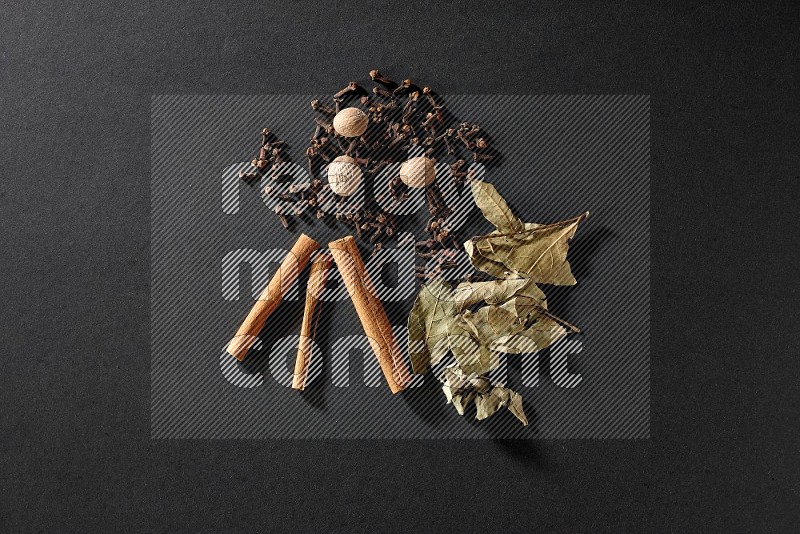 Cloves, ginger, bay laurel and cinnamon sticks on black flooring