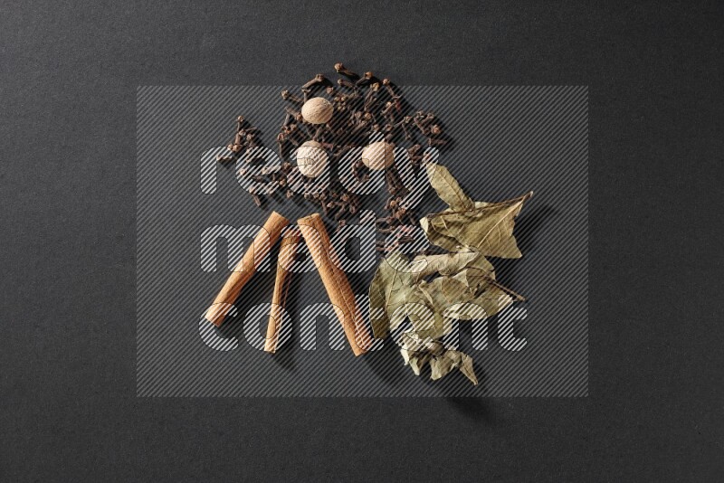 Cloves, ginger, bay laurel and cinnamon sticks on black flooring