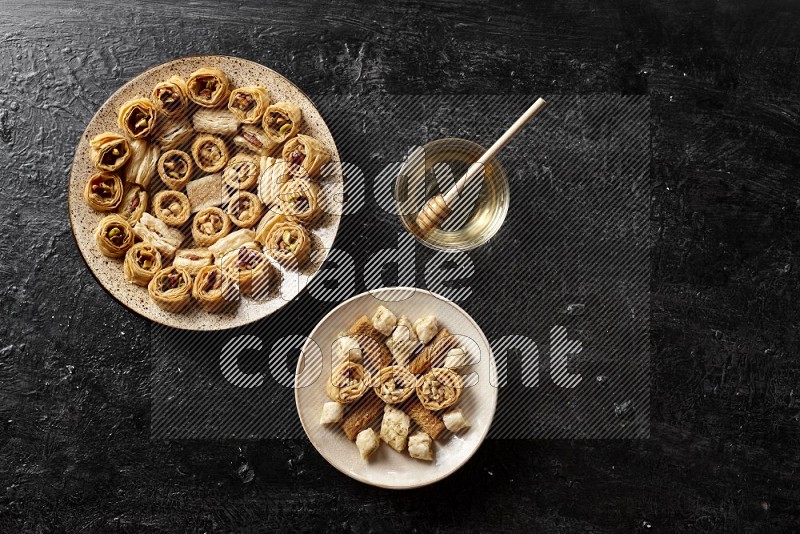 حلويات شرقية في أطباق فخارية مع العسل علي خلفية سوداء خشبية