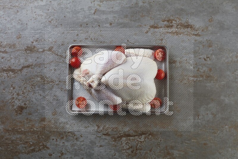 whole Raw chicken on a small oven trey direct on a rustic grey background